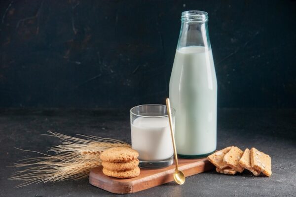top-view-delicious-milk-glass-bottle-golden-spoon-stacked-cookies-wooden-tray-spikes-dark-surface_140725-154552